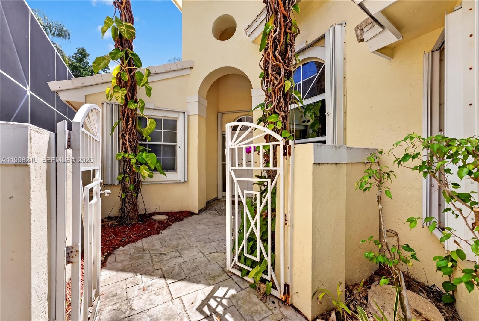 A paved walkway leads through a white metal gate to the entrance of a house — 1251 E Wilshire Cir E, Pembroke Pines FL 33027, PEMBROKE PINES, FL
