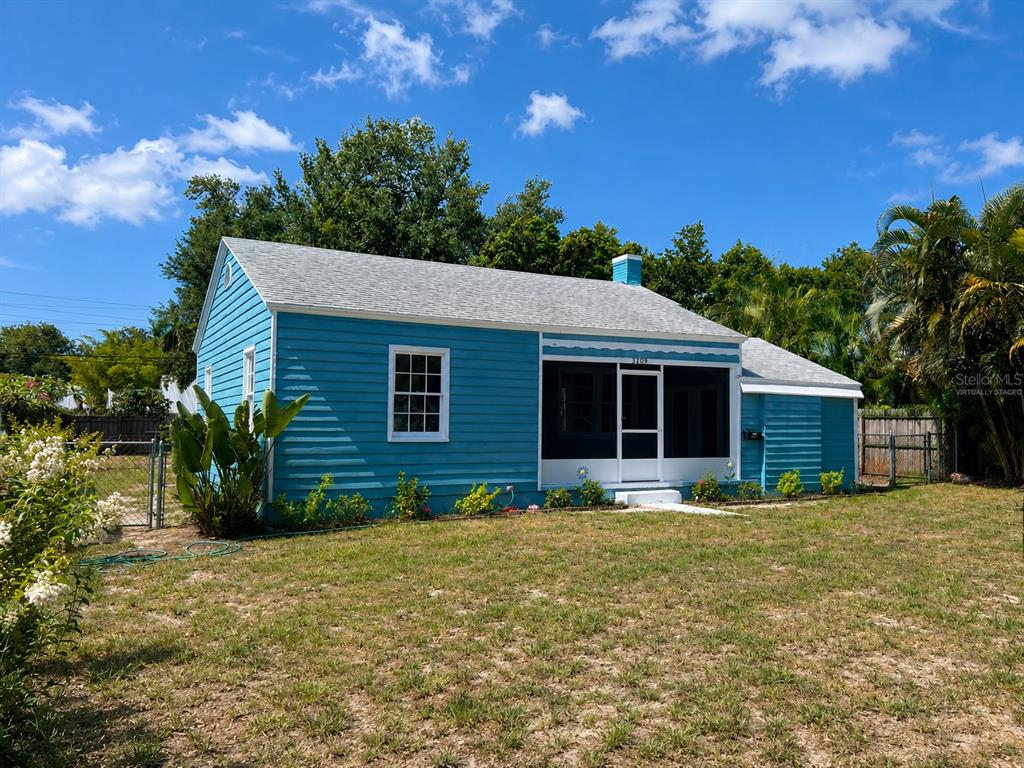 A blue, single-story house with a screened-in front porch stands on a grassy lot — 3209 AVENUE A W, BRADENTON, FL