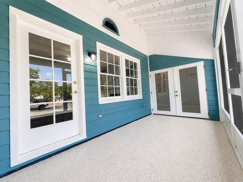 A covered porch features teal horizontal siding, white trim, glass doors, and a speckled floor — 3209 AVENUE A W, BRADENTON, FL