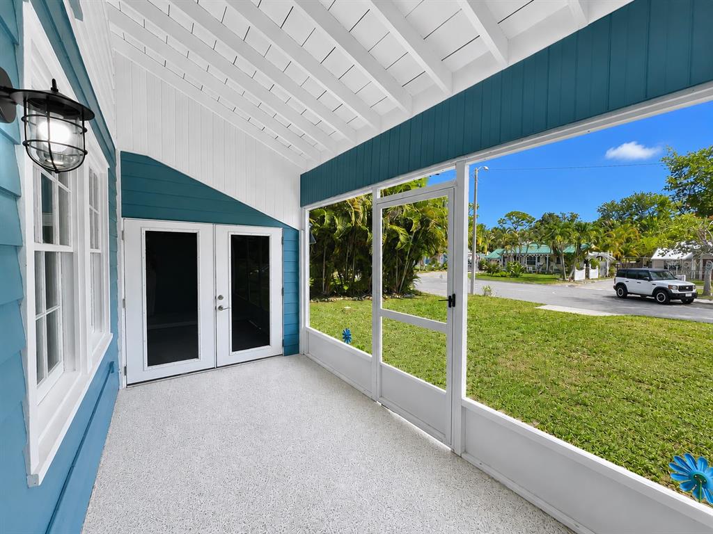 A screened-in porch features white flooring, blue siding, and a view of a residential street — 3209 AVENUE A W, BRADENTON, FL