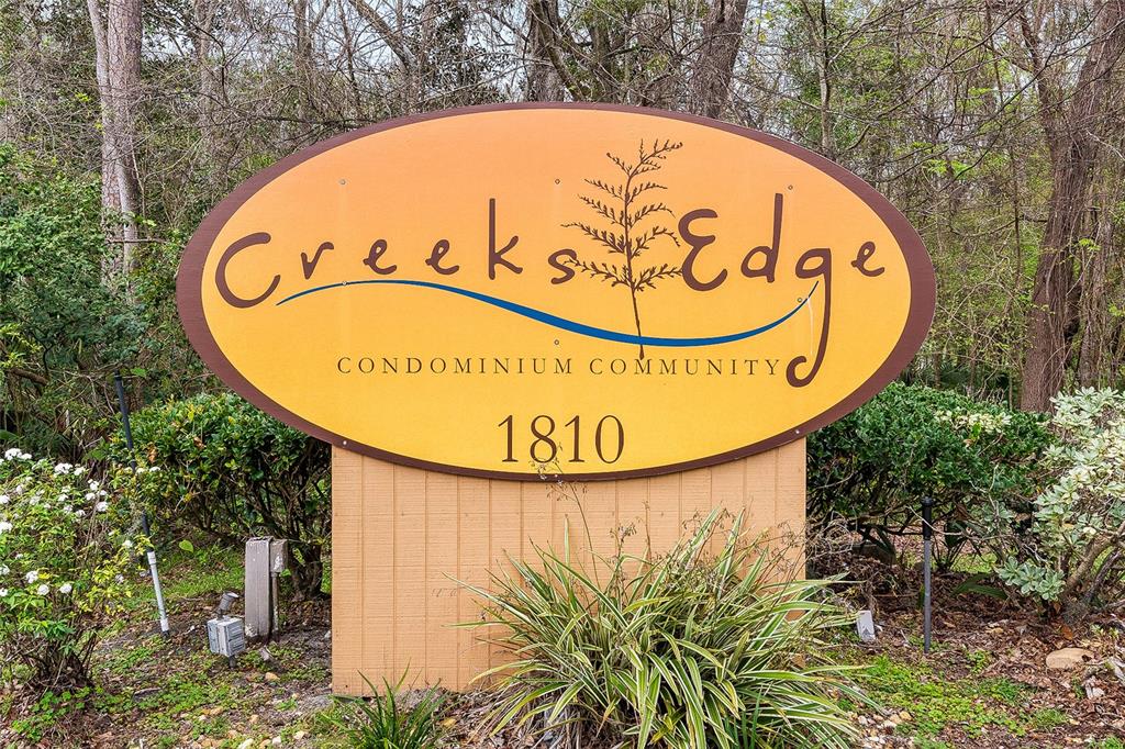 An oval sign for Creeks Edge Condominium Community stands in a wooded outdoor area — 1810 NW 23RD BOULEVARD Bldg 5, 211, GAINESVILLE, FL