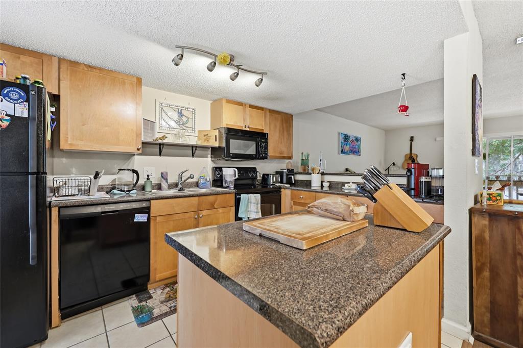 A kitchen features light wood cabinets, granite countertops, a central island, and black appliances — 1810 NW 23RD BOULEVARD Bldg 5, 211, GAINESVILLE, FL