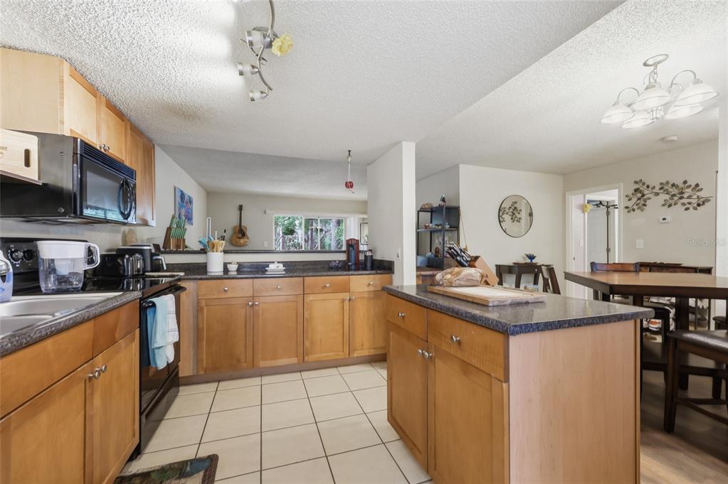 A kitchen features light wood cabinets, dark countertops, a center island, and tile flooring — 1810 NW 23RD BOULEVARD Bldg 5, 211, GAINESVILLE, FL