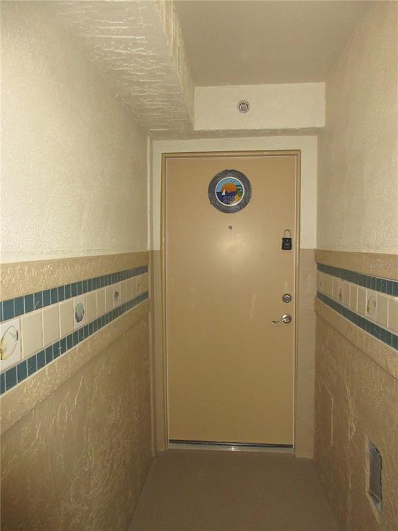 A beige door with a porthole window and a lockbox is centered in a hallway — 701 S ATLANTIC AVENUE UNIT 215, DAYTONA BEACH, FL