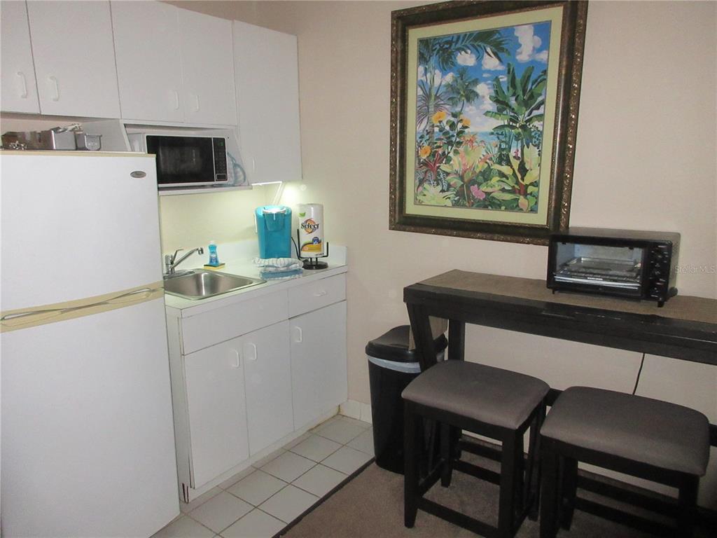 A small kitchen features white cabinets, a refrigerator, a sink, and a dining table — 701 S ATLANTIC AVENUE UNIT 215, DAYTONA BEACH, FL