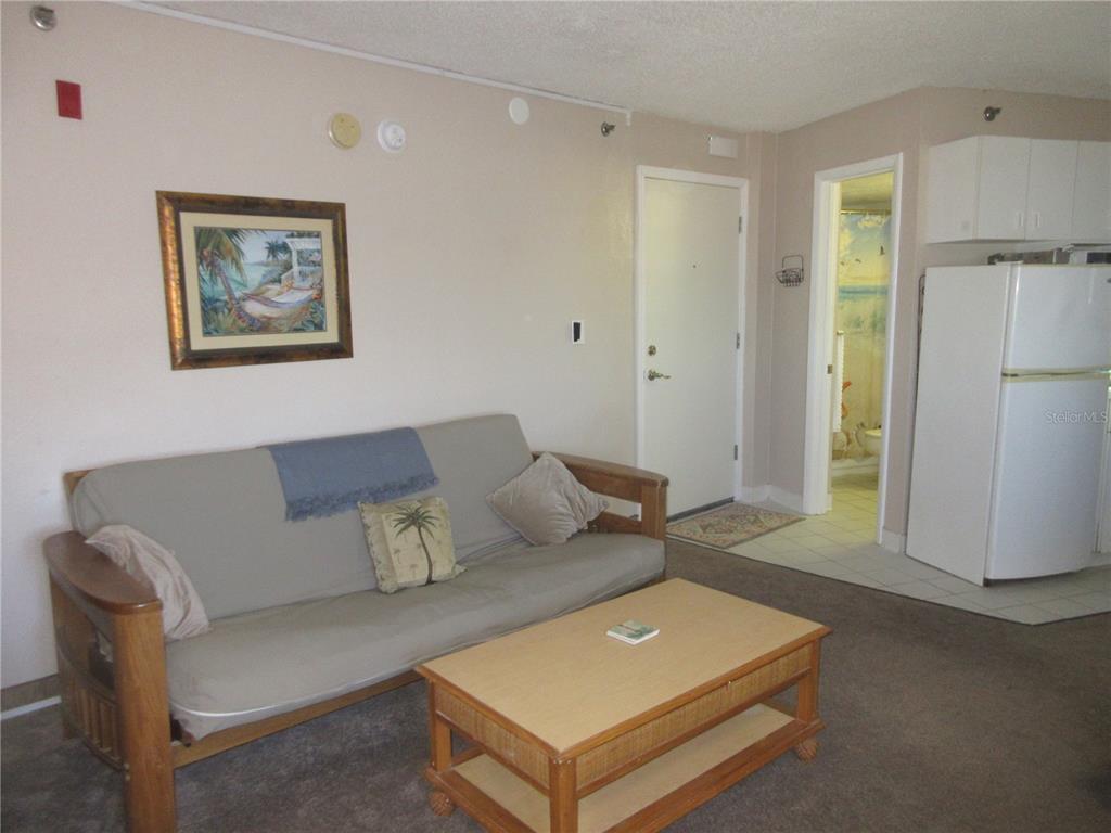 A living room features a futon, a wooden coffee table, and an adjacent kitchen area — 701 S ATLANTIC AVENUE UNIT 215, DAYTONA BEACH, FL