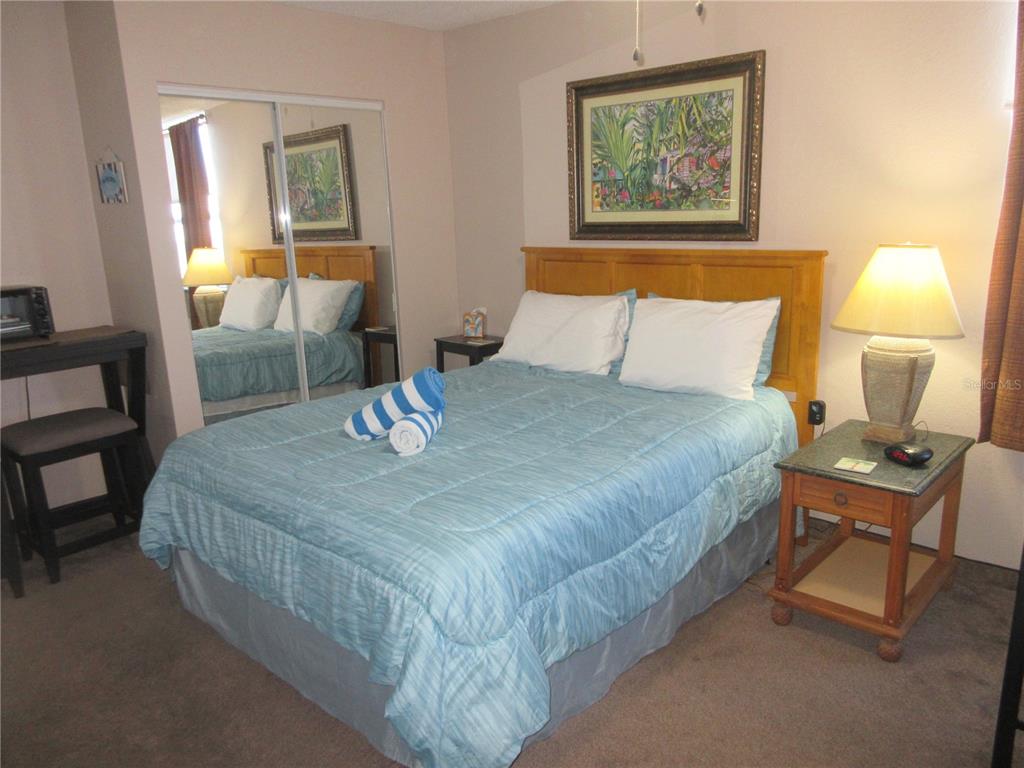 A bedroom features a bed with a blue comforter, a wooden headboard, and mirrored closet doors — 701 S ATLANTIC AVENUE UNIT 215, DAYTONA BEACH, FL