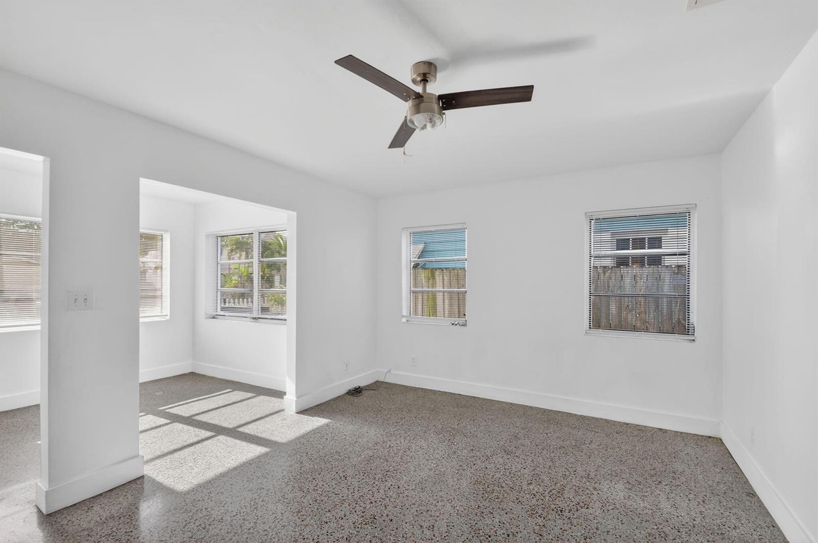 A bright, empty room with white walls, a ceiling fan, and speckled concrete flooring — 301 S L Street, FL 33460, FL