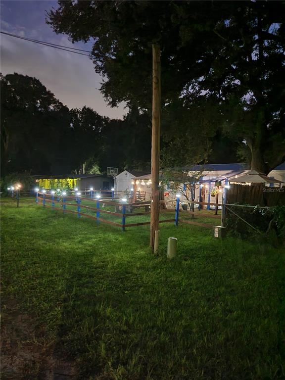 A grassy yard features a wooden fence with solar lights at dusk near a house — 12950 SE 104TH COURT, BELLEVIEW, FL