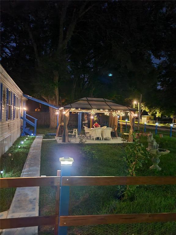 An illuminated outdoor gazebo with patio furniture sits in a yard next to a house — 12950 SE 104TH COURT, BELLEVIEW, FL
