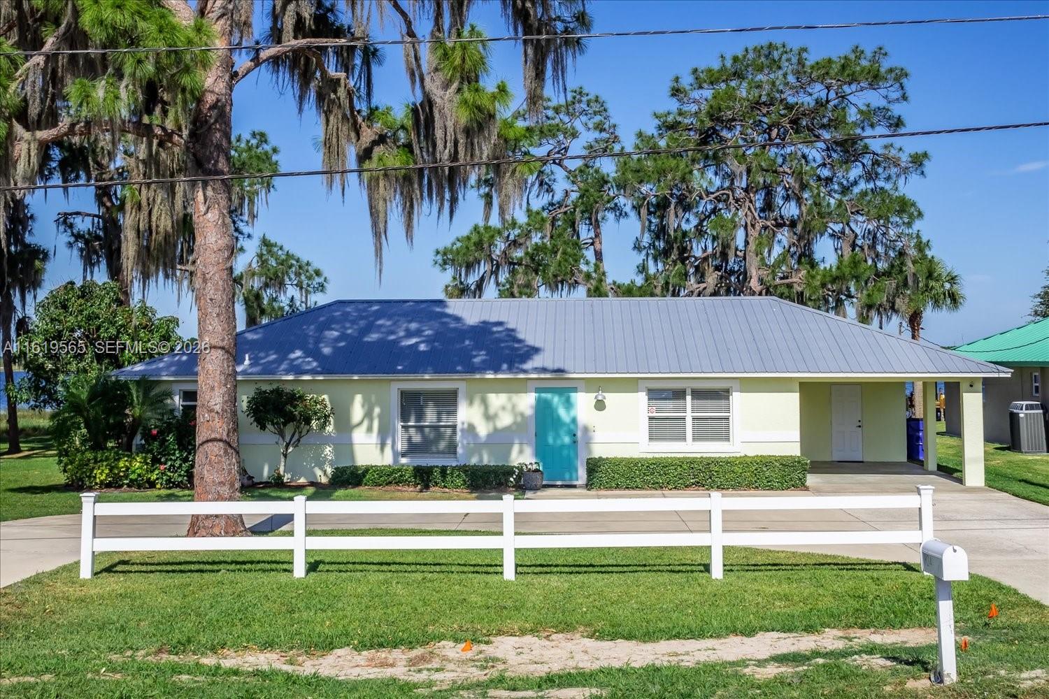 A single-story house with a light green exterior, metal roof, and white picket fence — 924 Lake Dr E, Lake Placid FL 33852, LAKE PLACID, FL