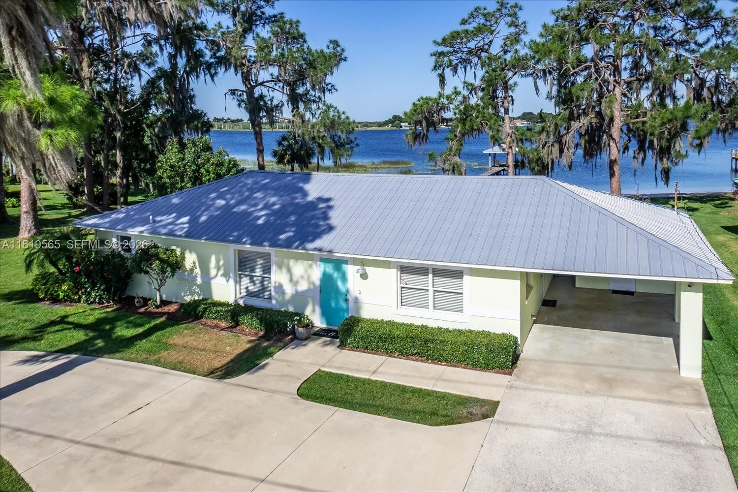 An aerial view shows a light-colored house with a metal roof and a carport — 924 Lake Dr E, Lake Placid FL 33852, LAKE PLACID, FL