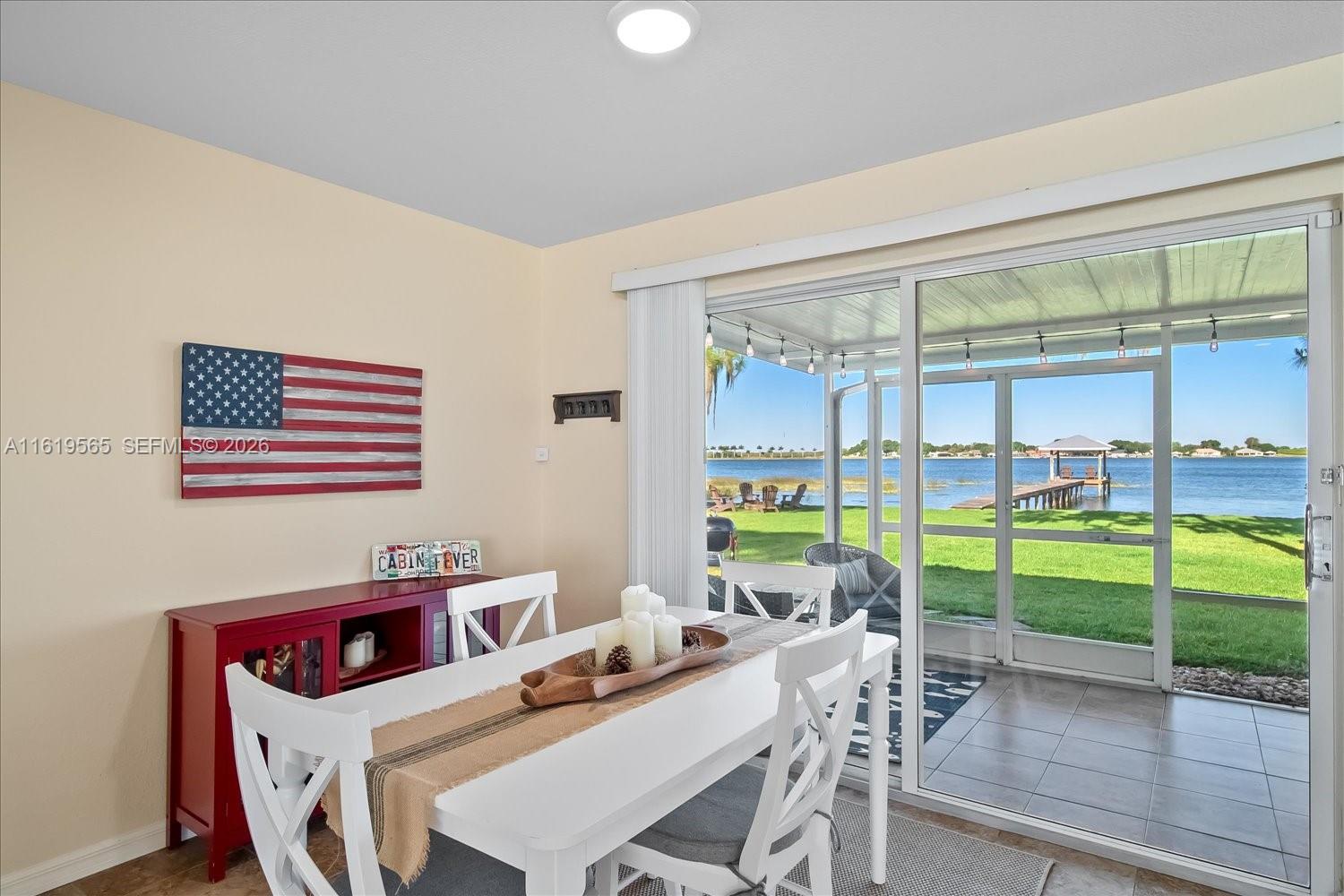 A dining area features a white table and chairs next to a sliding door overlooking a lake — 924 Lake Dr E, Lake Placid FL 33852, LAKE PLACID, FL