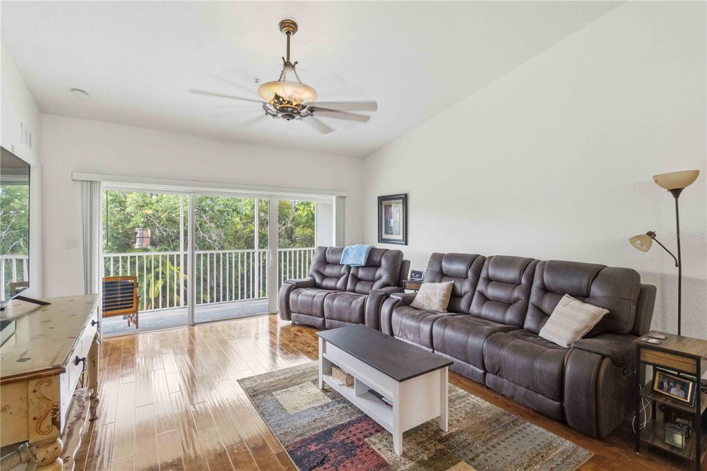 A living room features wood flooring, a ceiling fan, leather furniture, and a screened balcony — 7532 MARSH ORCHID CIRCLE UNIT 201, BRADENTON, FL