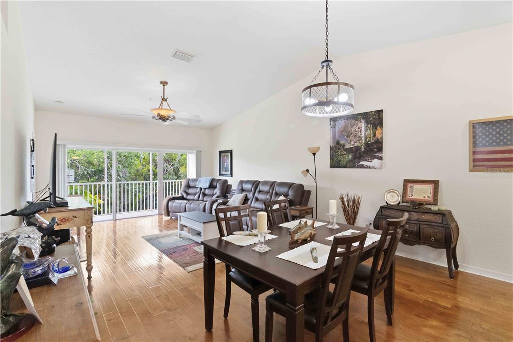 A dining area and living room with hardwood floors, a balcony, and a ceiling fan — 7532 MARSH ORCHID CIRCLE UNIT 201, BRADENTON, FL