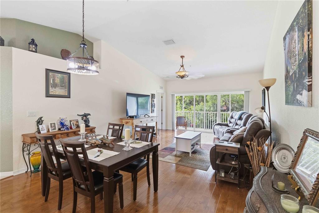 A dining and living area features hardwood floors, a vaulted ceiling, and a balcony view — 7532 MARSH ORCHID CIRCLE UNIT 201, BRADENTON, FL