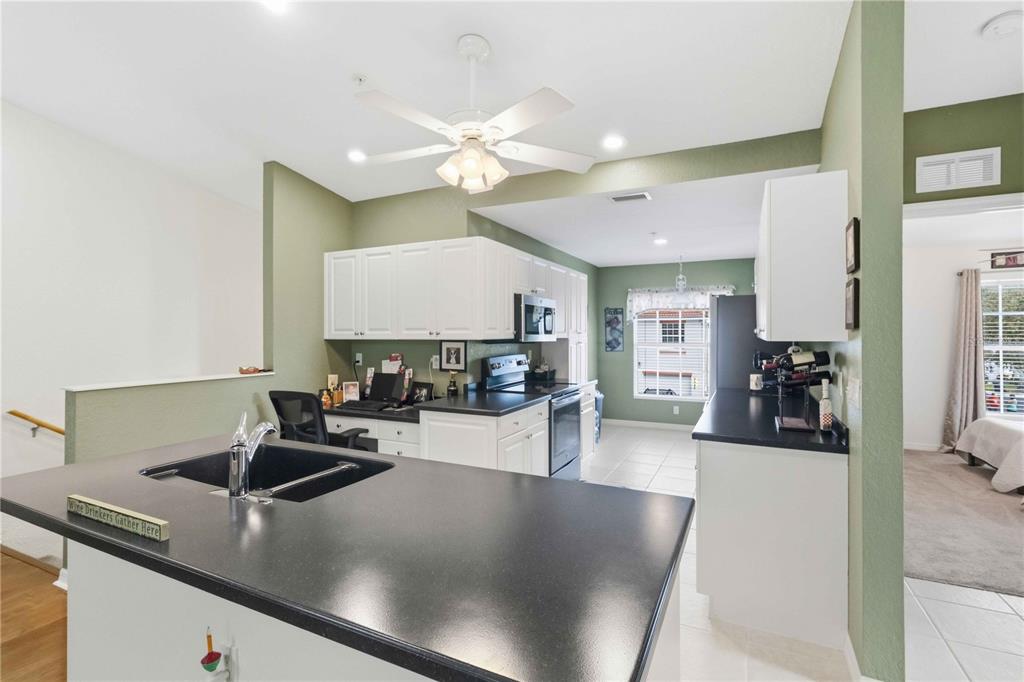 A kitchen features white cabinets, black countertops, a ceiling fan, and an adjacent office nook — 7532 MARSH ORCHID CIRCLE UNIT 201, BRADENTON, FL