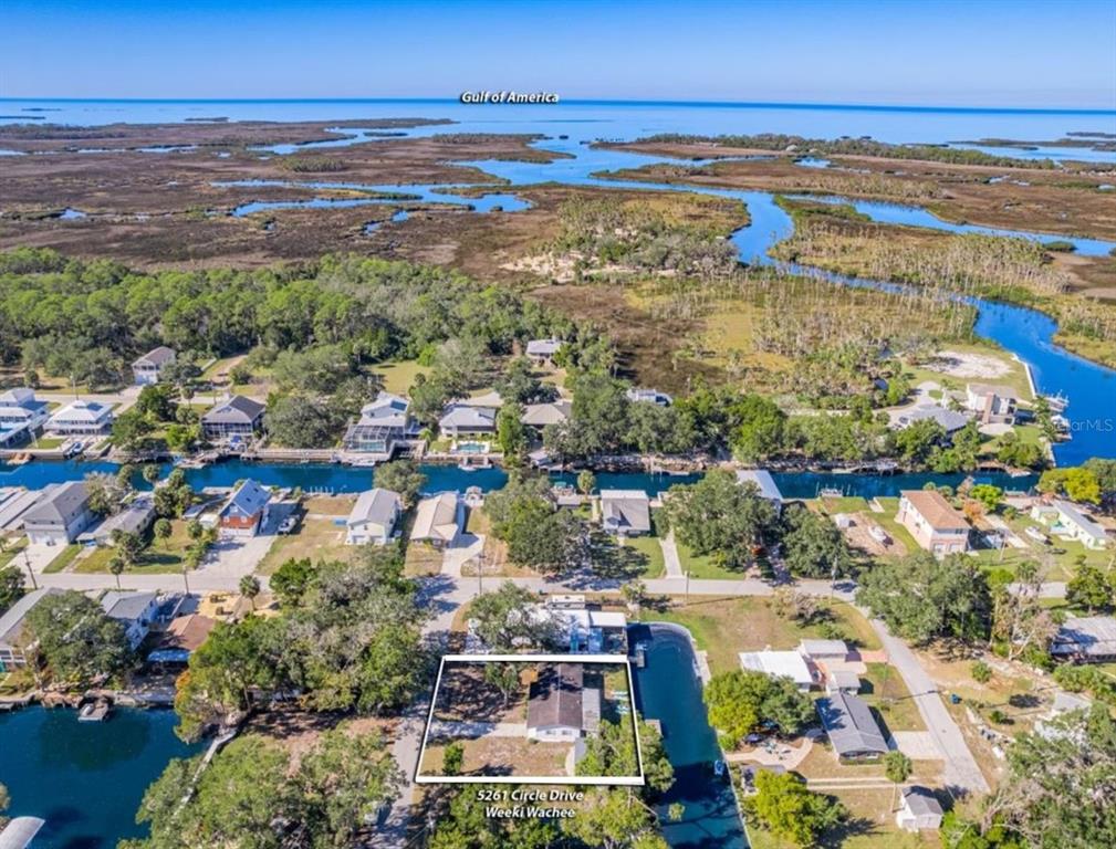 An aerial view shows a waterfront house with a canal and marshland in the background — 5261 CIRCLE DRIVE, WEEKI WACHEE, FL