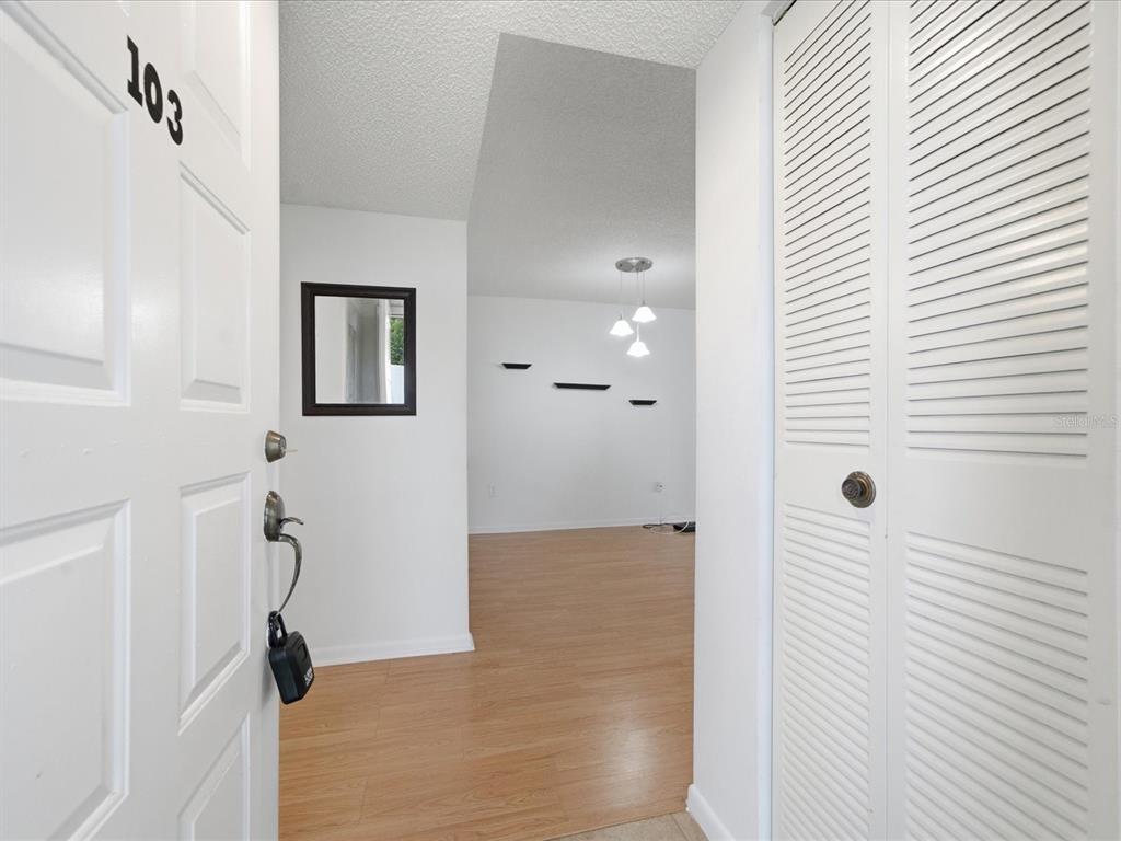 An open front door reveals a hallway with light wood flooring and a white closet — 12130 SPARTAN WAY UNIT 103, HUDSON, FL
