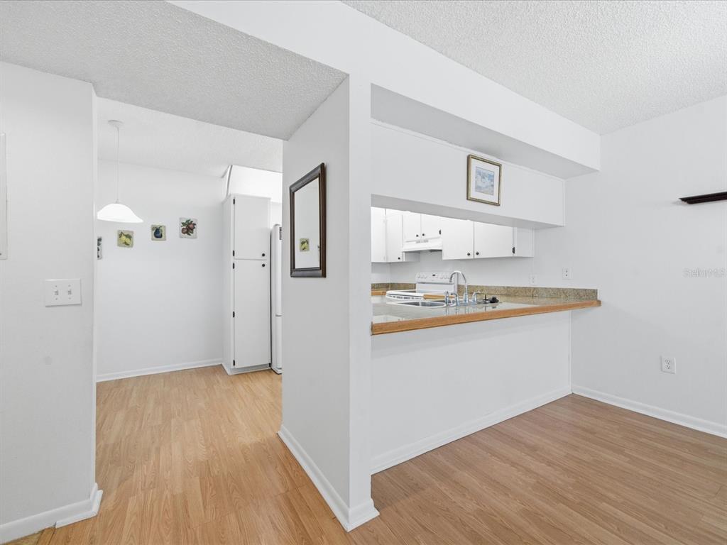 A kitchen with a breakfast bar overlooks a dining area with light wood-look flooring — 12130 SPARTAN WAY UNIT 103, HUDSON, FL