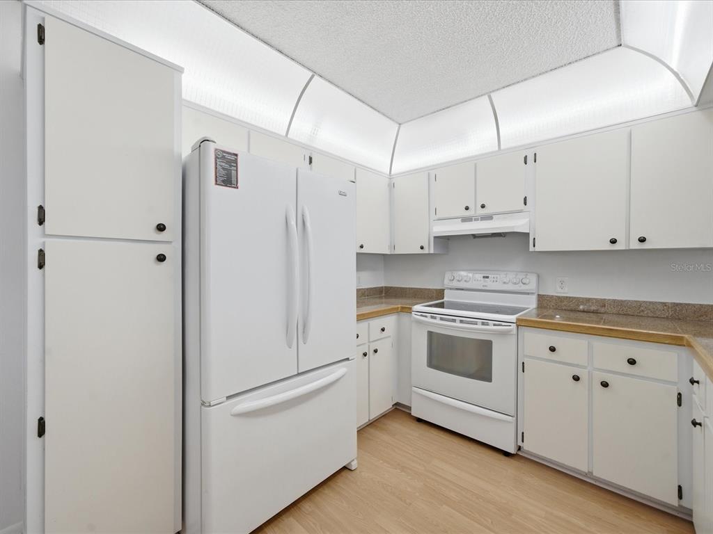 A kitchen with white cabinets, white appliances, and light wood-look flooring — 12130 SPARTAN WAY UNIT 103, HUDSON, FL