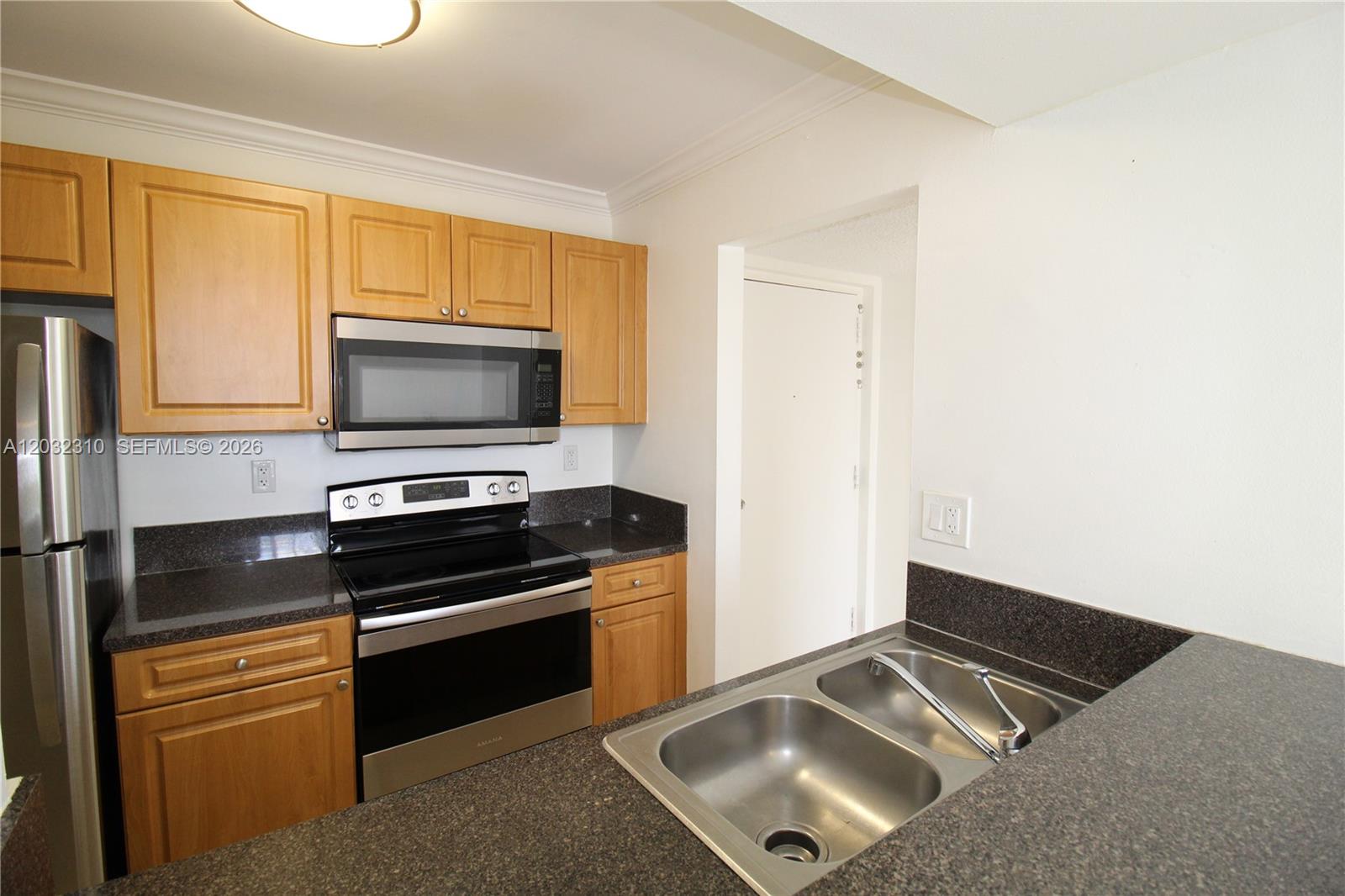 A kitchen features light wood cabinets, dark countertops, stainless steel appliances, and a double sink — HIALEAH, FL