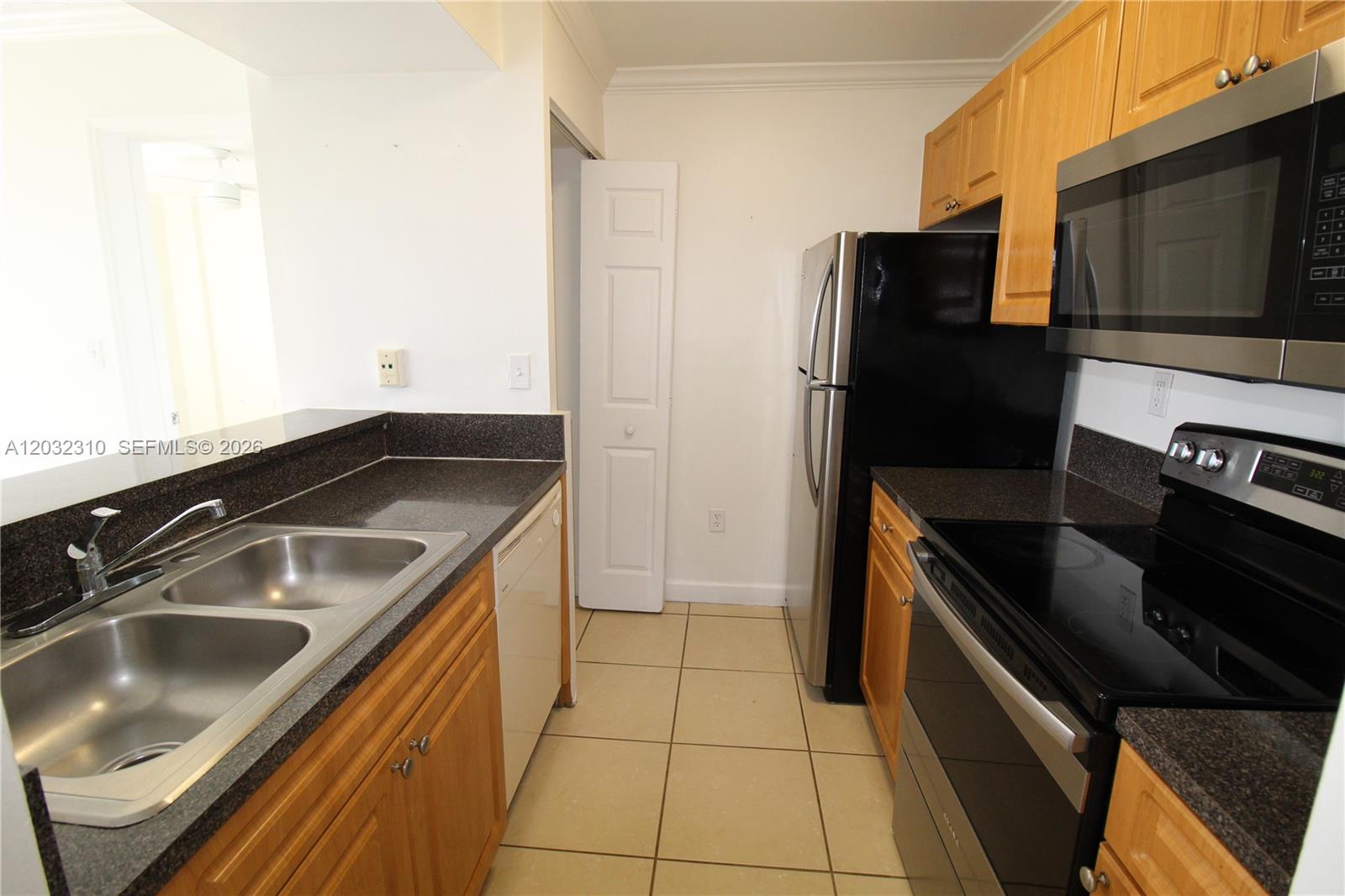 A kitchen features light wood cabinets, dark countertops, stainless steel appliances, and tile flooring — HIALEAH, FL