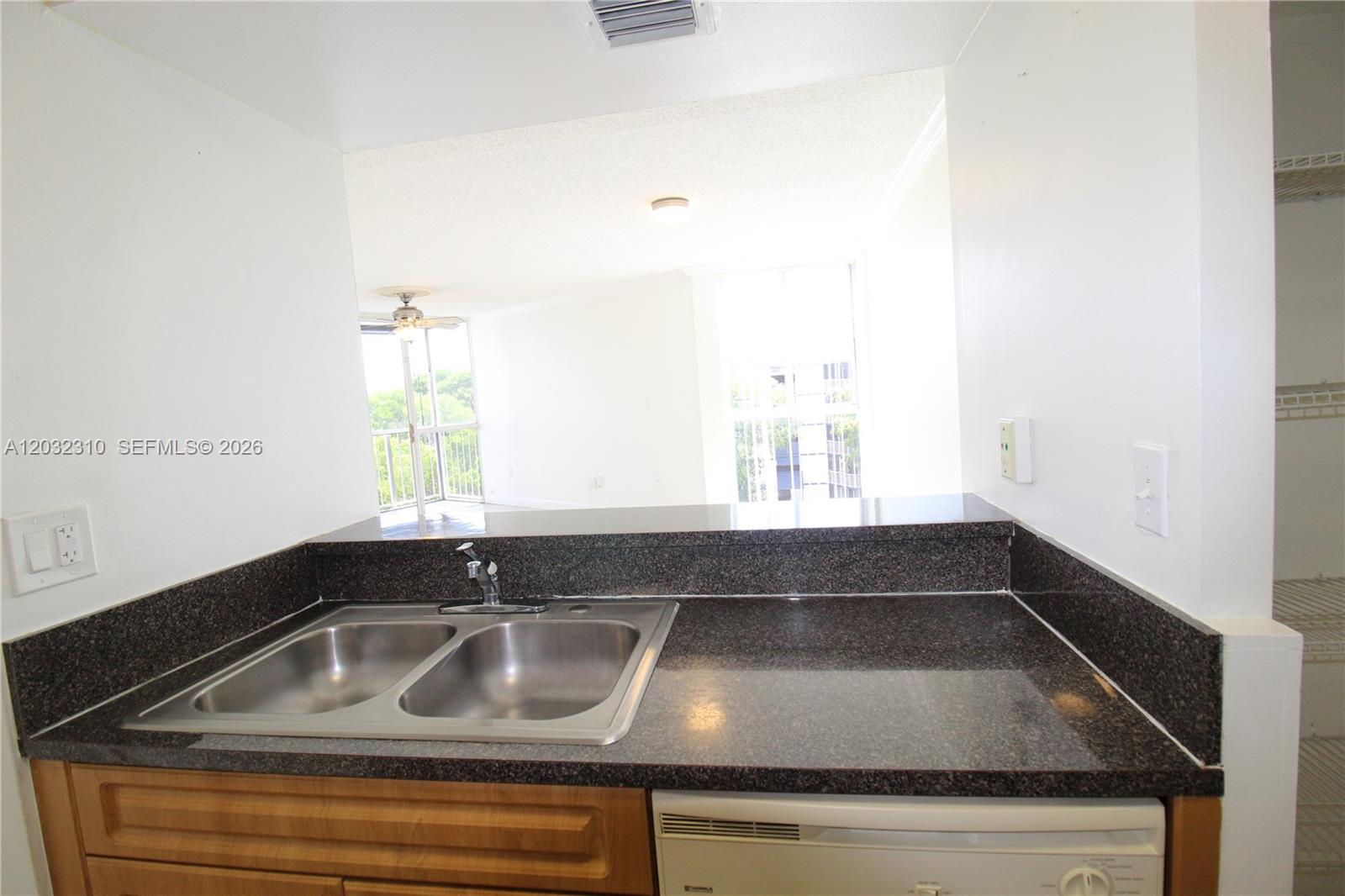 A kitchen sink with dark granite countertops overlooks a bright living area and balcony — HIALEAH, FL