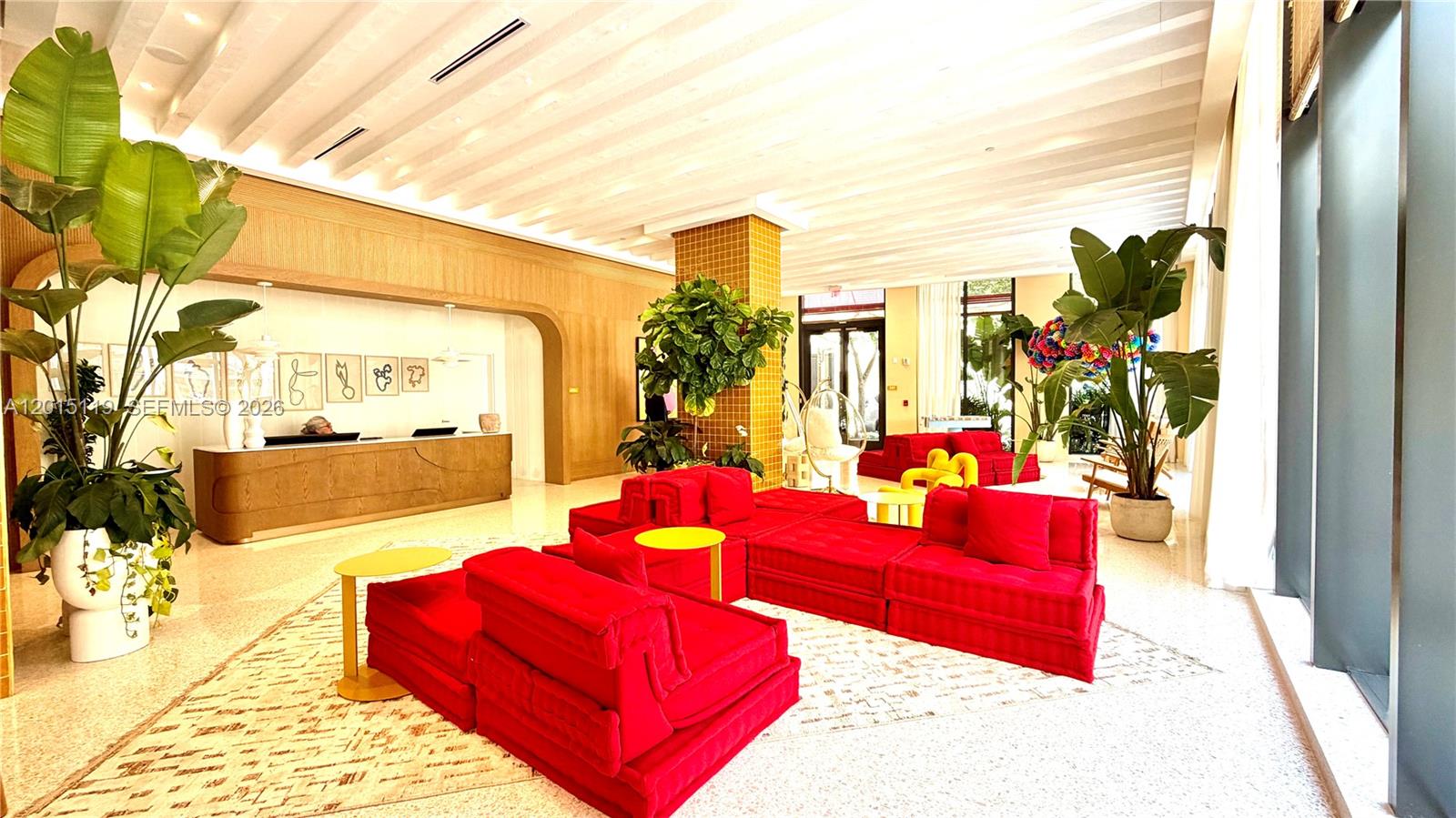 A hotel lobby features bright red modular seating, large potted plants, and a wooden reception desk — 90 NE 32nd St # 1125, Miami FL 33127, MIAMI, FL