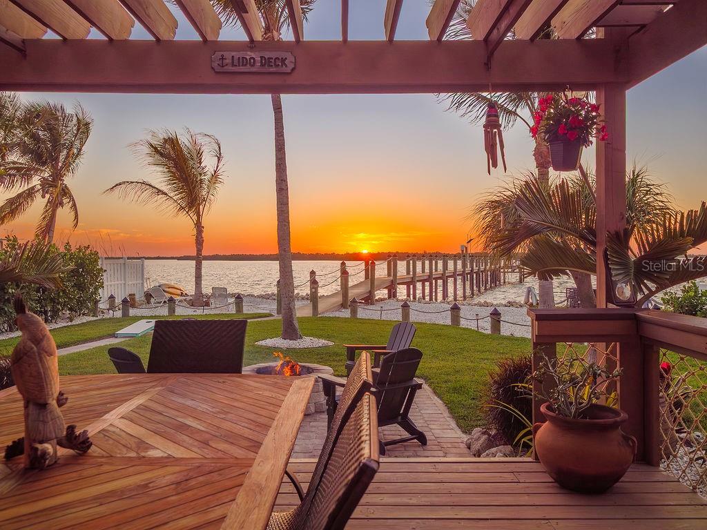 A wooden deck with a fire pit overlooks a sunset view of the water — 3 MICHIANA PLACE, TERRA CEIA, FL