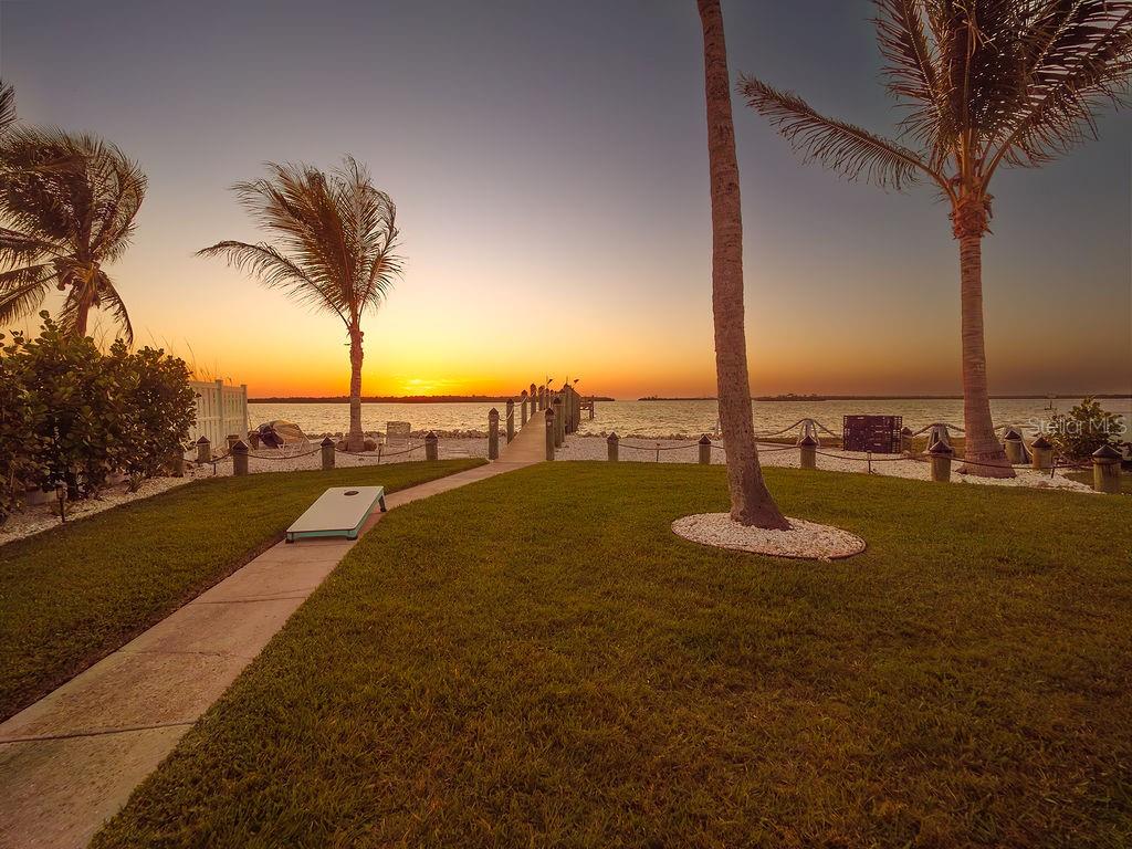 A grassy lawn with a cornhole board leads to a wooden pier at sunset — 3 MICHIANA PLACE, TERRA CEIA, FL