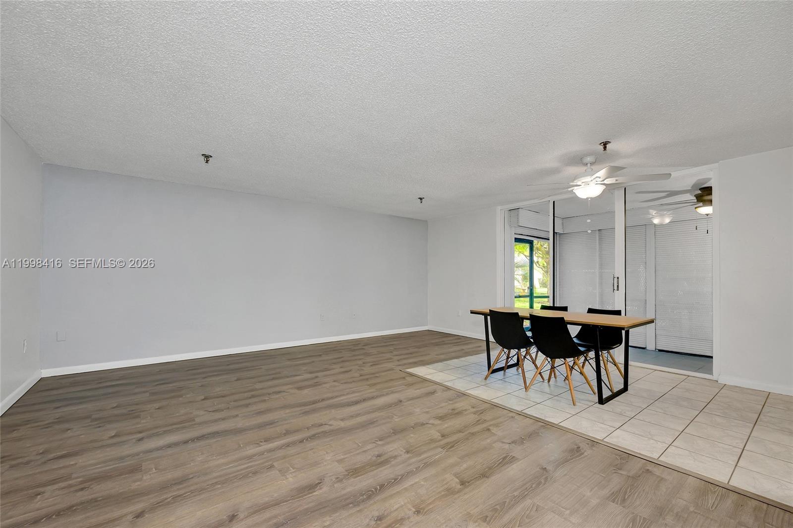 A dining area with a table and chairs sits on tiled flooring beside wood-look floors — 671 NE 195th St # 114E, Miami FL 33179, MIAMI, FL