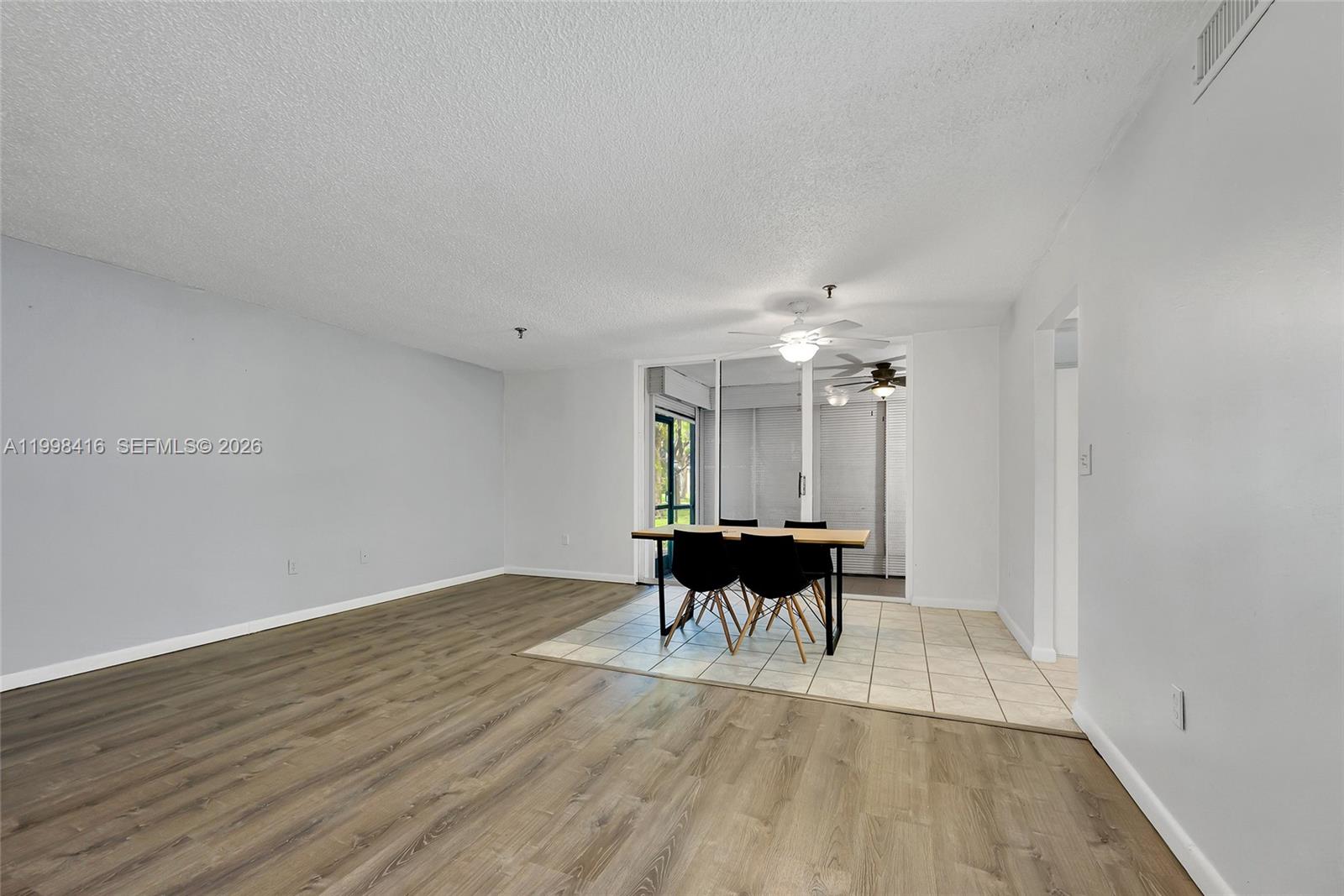 A dining area with a table and chairs sits on tiled flooring beside wood-look floors — 671 NE 195th St # 114E, Miami FL 33179, MIAMI, FL