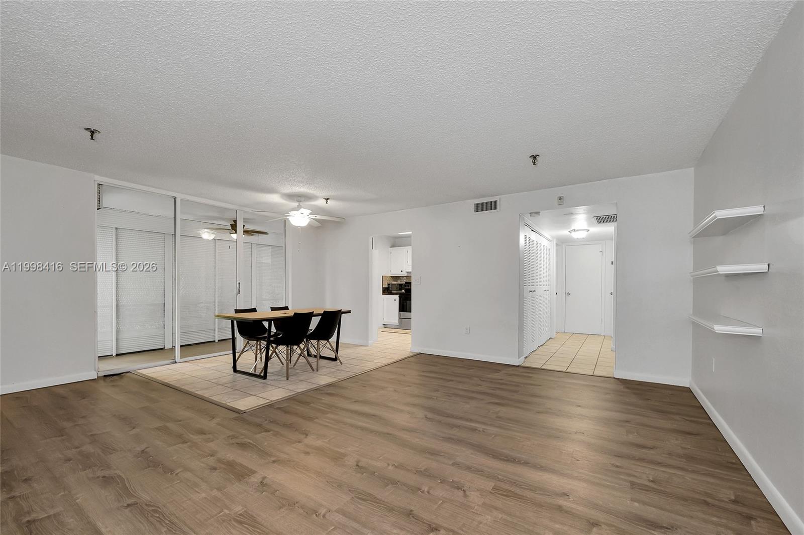 An open-concept living and dining area features wood-look flooring, white walls, and sliding glass doors — 671 NE 195th St # 114E, Miami FL 33179, MIAMI, FL