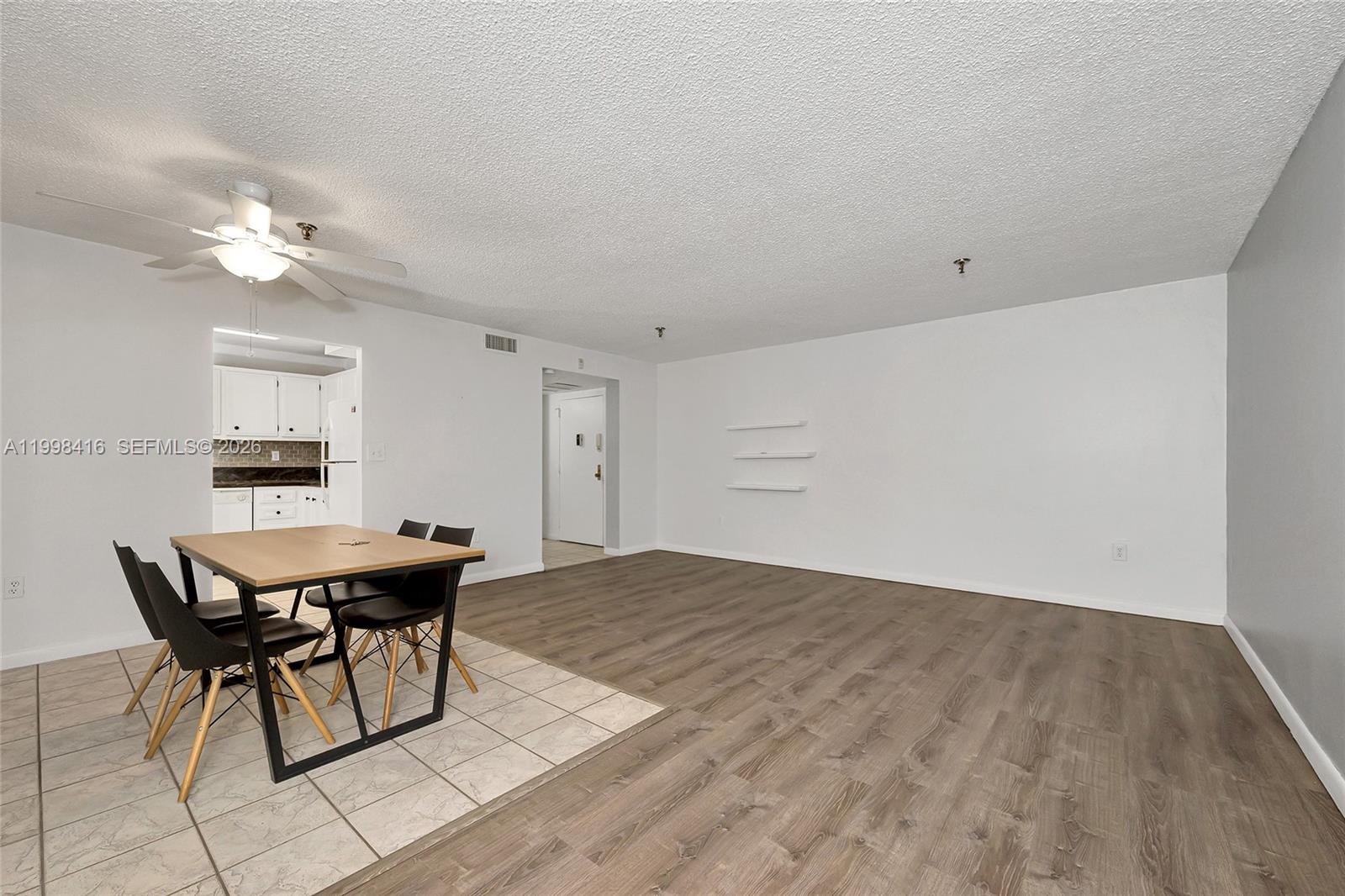 A dining area with tile flooring transitions into a living space with wood-look laminate floors — 671 NE 195th St # 114E, Miami FL 33179, MIAMI, FL