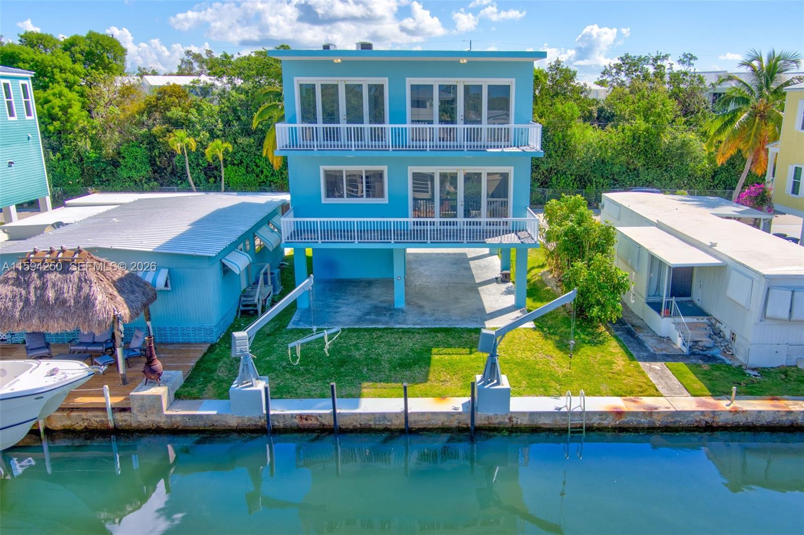 A bright blue, three-story waterfront home features two boat lifts and a private dock — 84 Coral Way, Key Largo FL 33037, KEY LARGO, FL