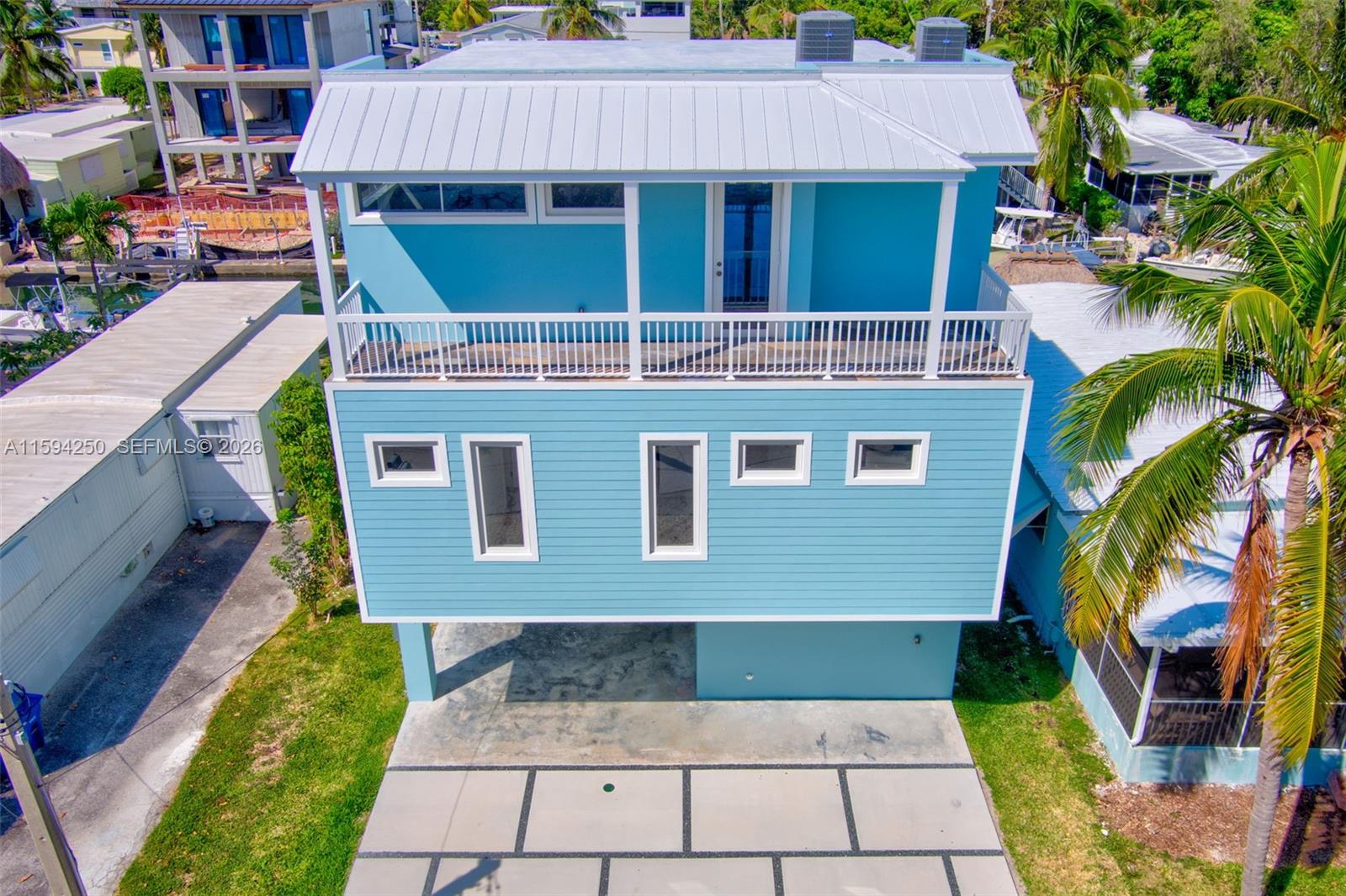 An elevated light blue house with a white metal roof and a large balcony — 84 Coral Way, Key Largo FL 33037, KEY LARGO, FL