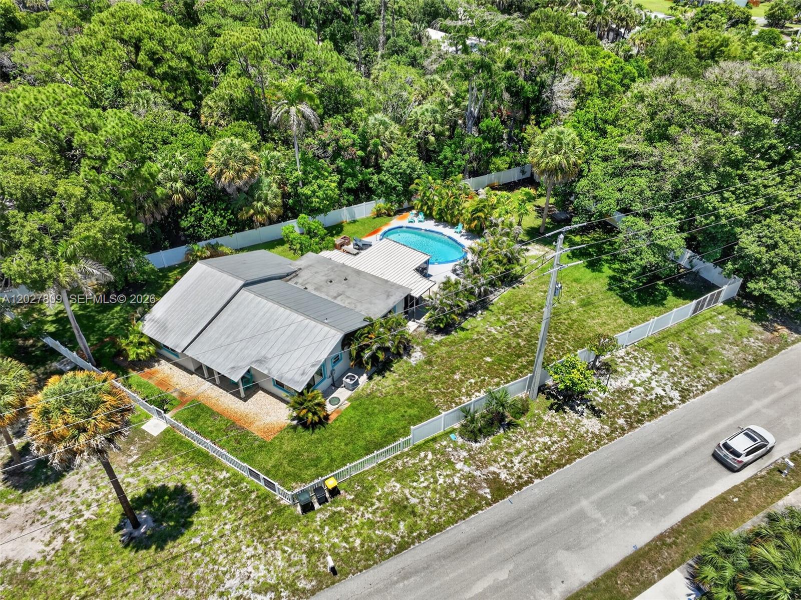 An aerial view shows a house with a metal roof, a backyard pool, and a fenced yard — 1023 SE 7th St, Stuart FL 34996, STUART, FL