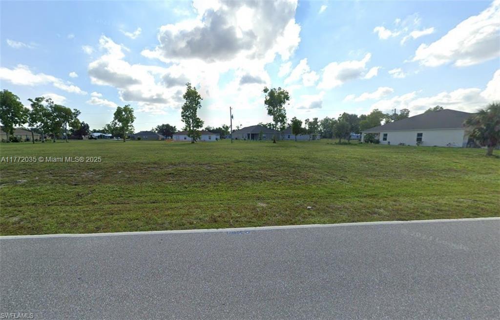 A vacant, grassy residential lot is shown from the street with houses in the background — 25482 Doredo Dr, Punta Gorda FL 33955, PUNTA GORDA, FL