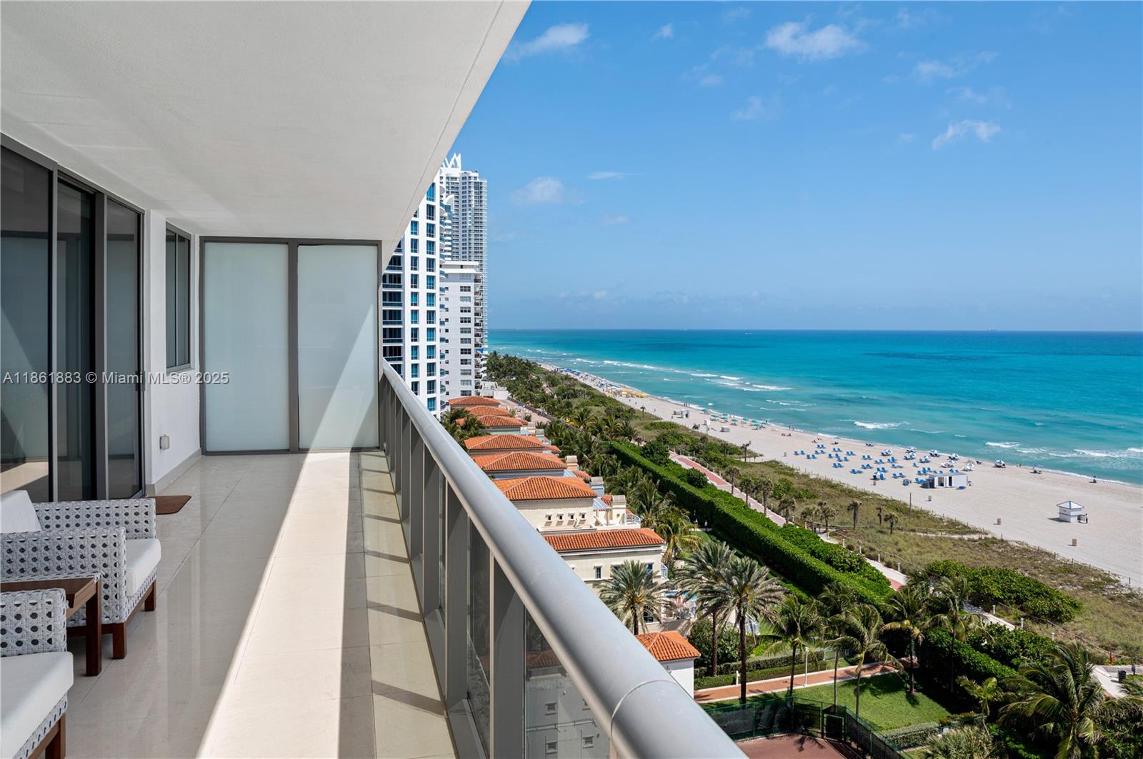 A balcony with outdoor seating overlooks a sandy beach, ocean, and nearby high-rise buildings — 5875 Collins Ave # 1202, Miami Beach FL 33140, MIAMI BEACH, FL