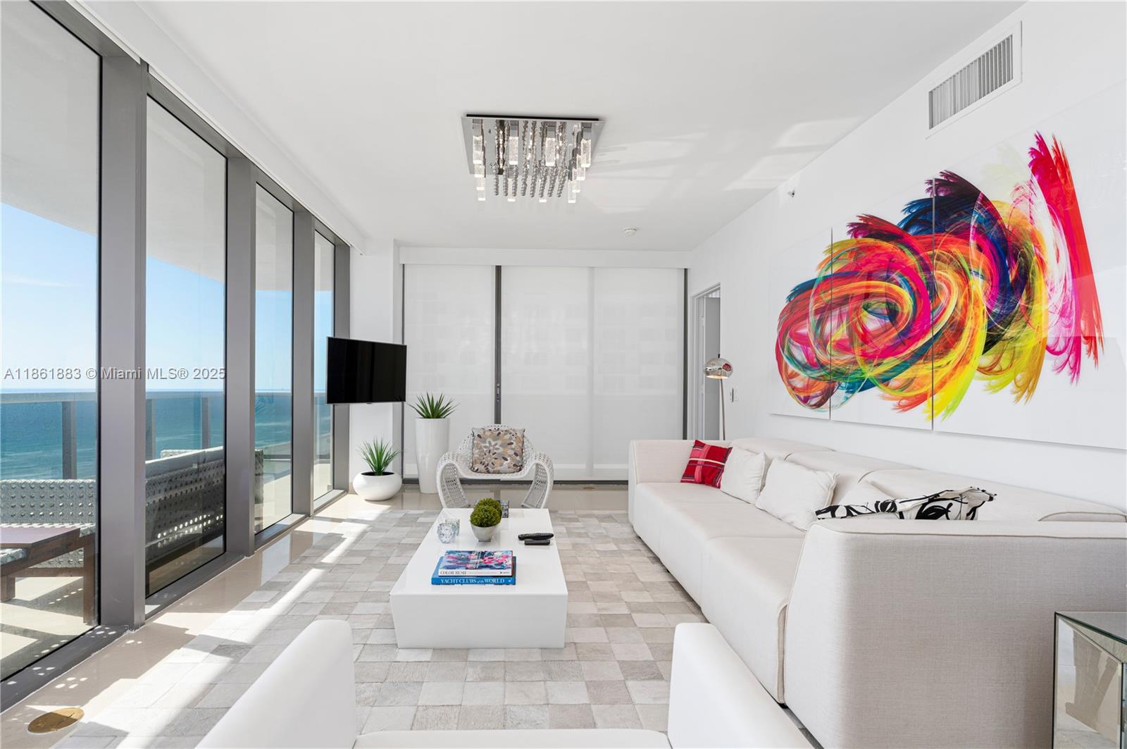 A bright living room features a white sofa, a coffee table, and ocean views — 5875 Collins Ave # 1202, Miami Beach FL 33140, MIAMI BEACH, FL