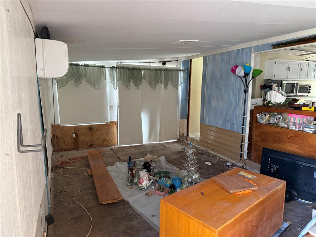 An unfinished room features exposed subflooring, wood-paneled walls, a window with valances, and a television — 2601 GULF DRIVE N UNIT 502, BRADENTON BEACH, FL