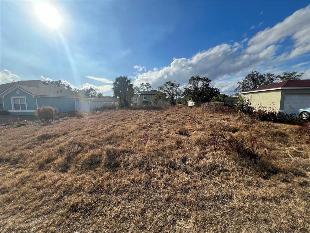 A vacant, grassy residential lot sits between two existing houses under a sunny sky — 1608 REDFIN DRIVE, KISSIMMEE, FL