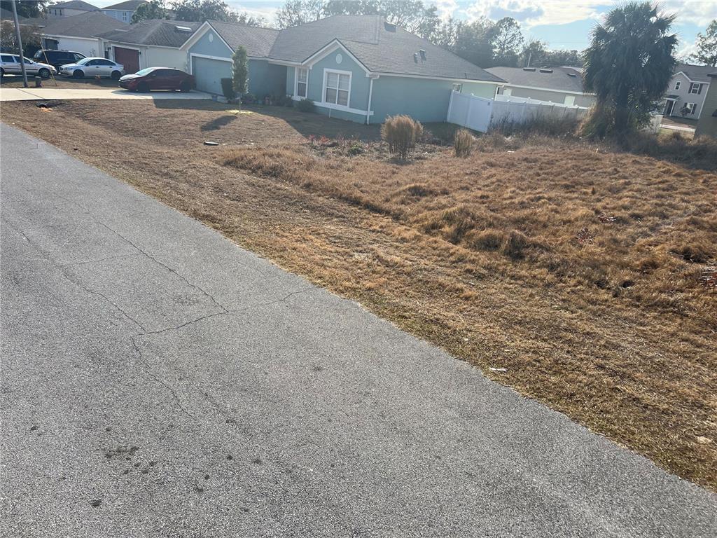 A view of a vacant, dry grassy lot next to a suburban house and street — 1608 REDFIN DRIVE, KISSIMMEE, FL