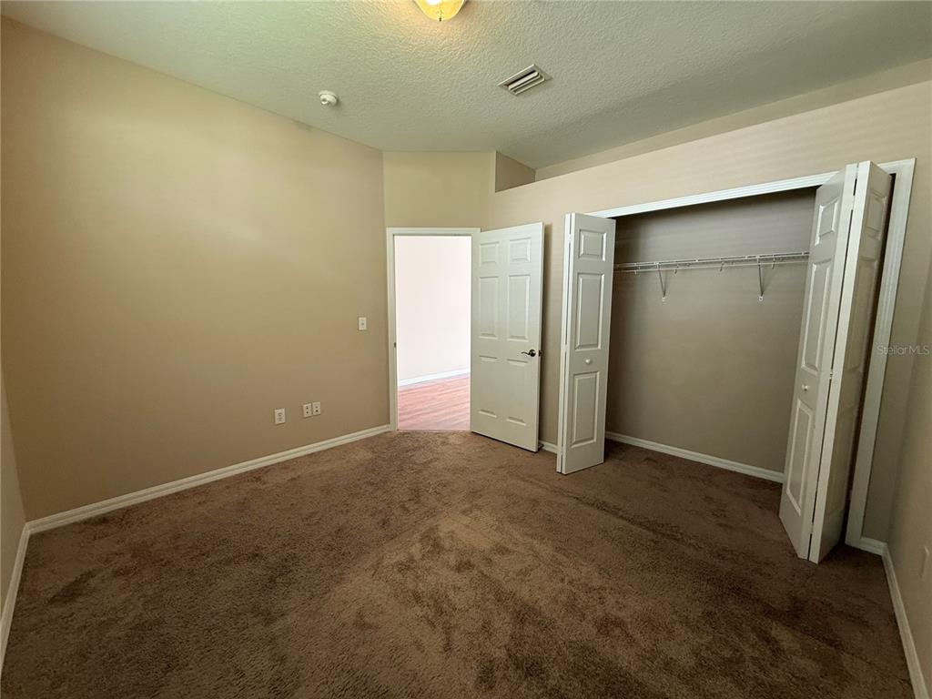 A bedroom with tan walls, brown carpet, a closet with bifold doors, and an open doorway — 6520 BRIDGECREST DRIVE, LITHIA, FL