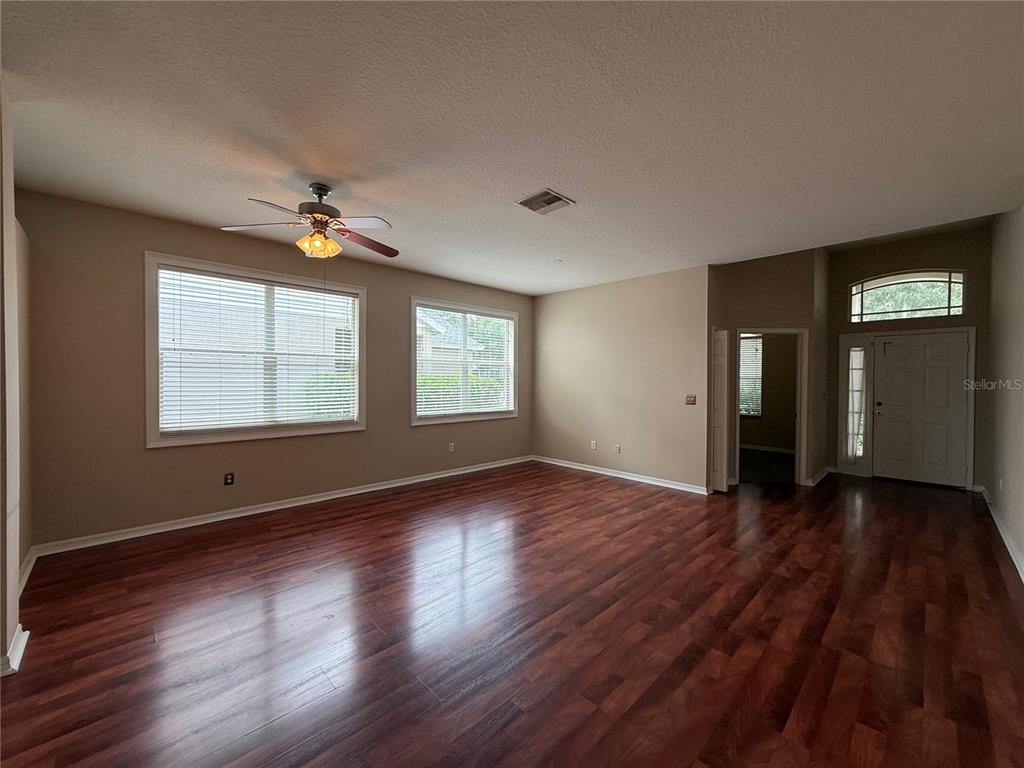 A spacious living room features dark wood-look flooring, beige walls, and a ceiling fan — 6520 BRIDGECREST DRIVE, LITHIA, FL