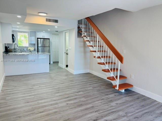 An open-concept kitchen and living area features light wood-look flooring and a wooden staircase — 5650 W 26th Ct # 206, Hialeah FL 33016, HIALEAH, FL