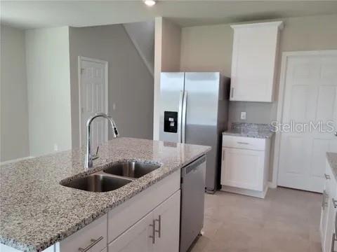 A kitchen features a granite-topped island with a sink, stainless steel appliances, and white cabinetry — 4031 PUCOLO WAY, DAVENPORT, FL