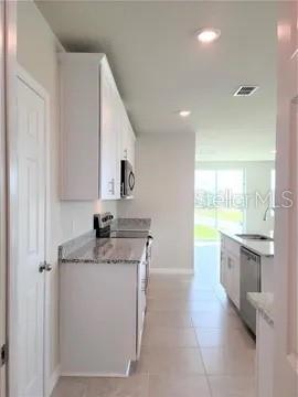 A kitchen features white cabinets, granite countertops, and light tile flooring — 4031 PUCOLO WAY, DAVENPORT, FL