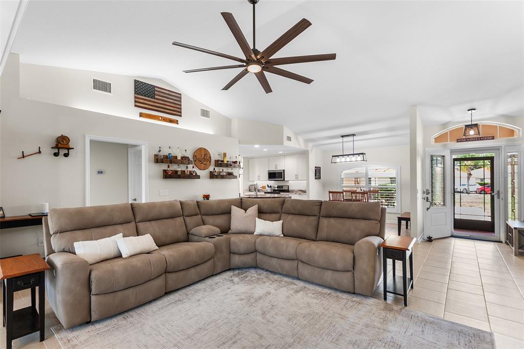 A spacious living room features a large sectional sofa, a ceiling fan, and an open kitchen — 120 MORNING GLORY CIRCLE, WINTER HAVEN, FL